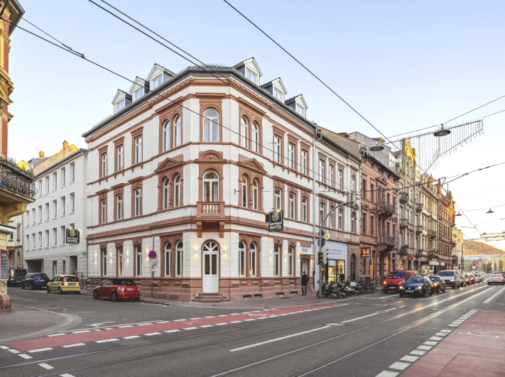 Dieses Bild zeigt das Wohnzimmer in der Villa von Milla Estate. Es hat einen grünlichen Fliesenboden mit Marmoroptik. Einen Esstisch mit 6 Stühlen, ein graues Sofa und einen großen Flachbild Fernsehr an der Wand. Am Ende des Raumes befindet sich eine Panoramafenster-Tür als Zugang zur Terrasse und Garten.